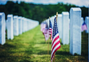 Rows of military tombstone with flags placed in front of them.